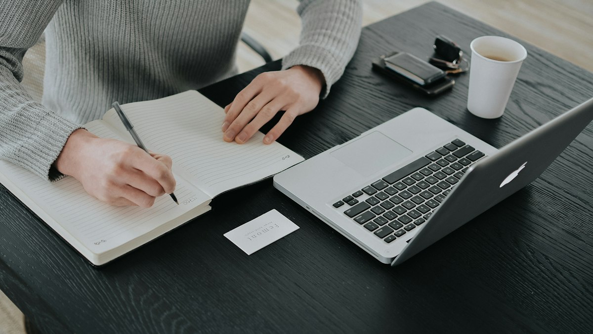 Personne rédigeant des notes dans un carnet à son bureau